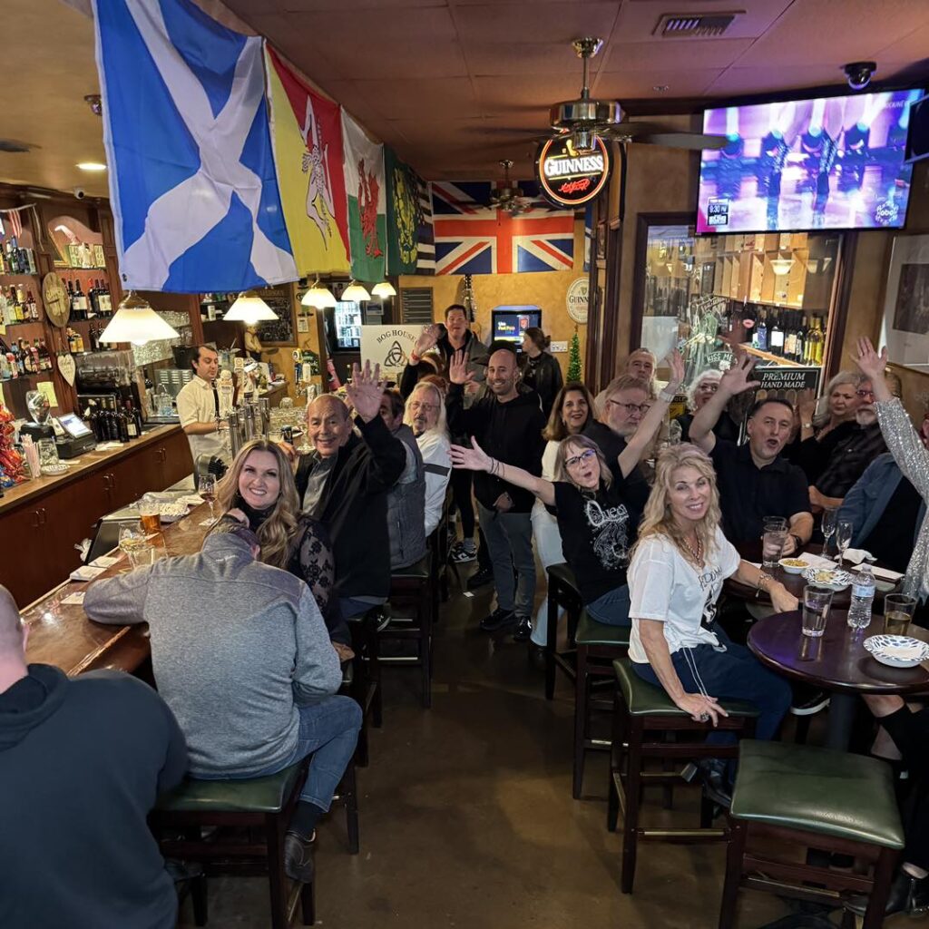 A lively bar scene featuring a group of friends sitting together, with colorful flags displayed around them.